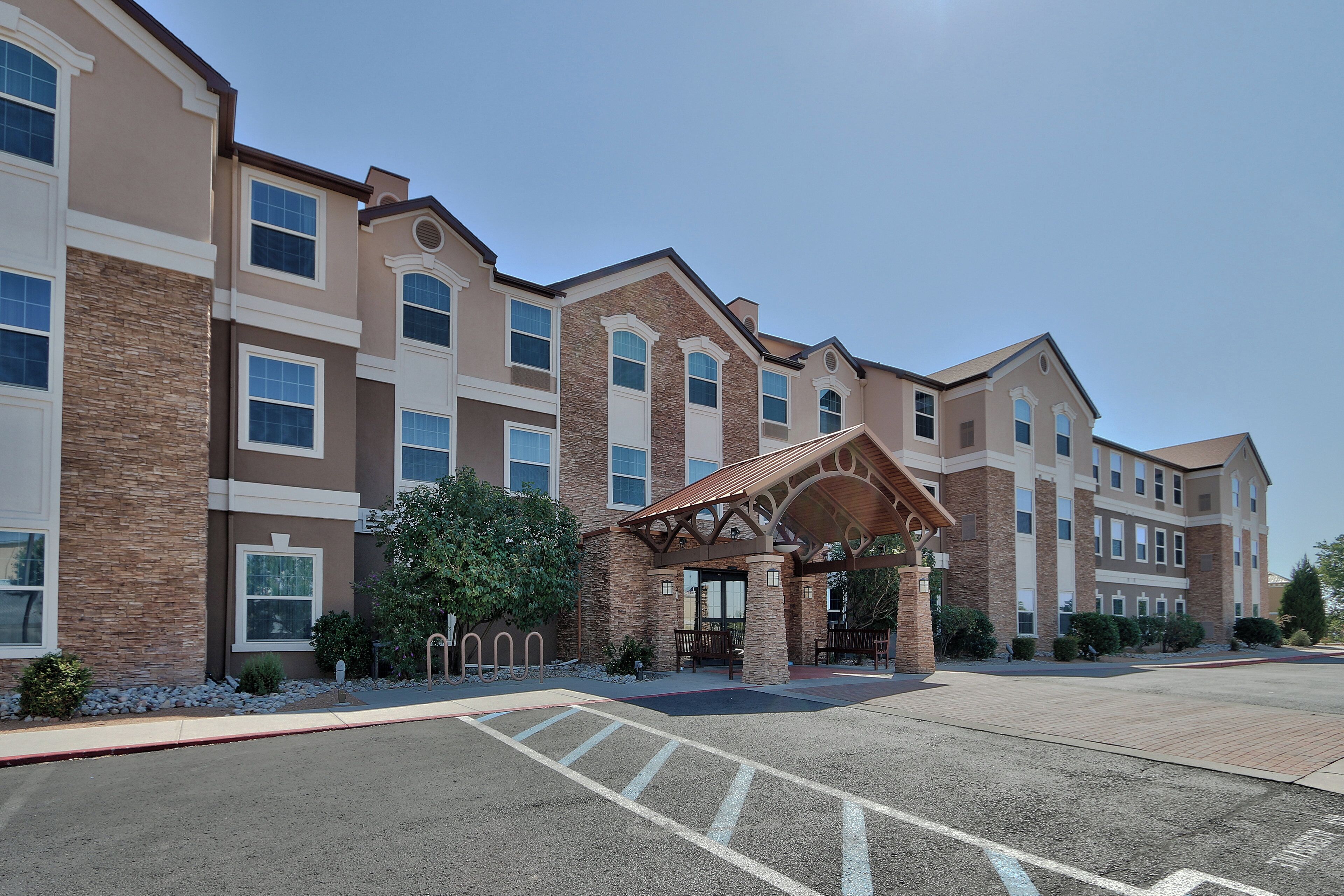 A multi-story hotel with a central entrance, stone facade, and a parking lot.