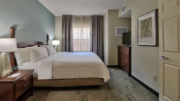 A hotel room with a bed, a nightstand, a lamp, a dresser, a framed picture on the wall, and a window with curtains.