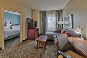 A hotel room with a bed, a desk, a sofa, a TV, and a window with curtains. - Staybridge Suites North - Albuquerque by IHG (Albuquerque)
