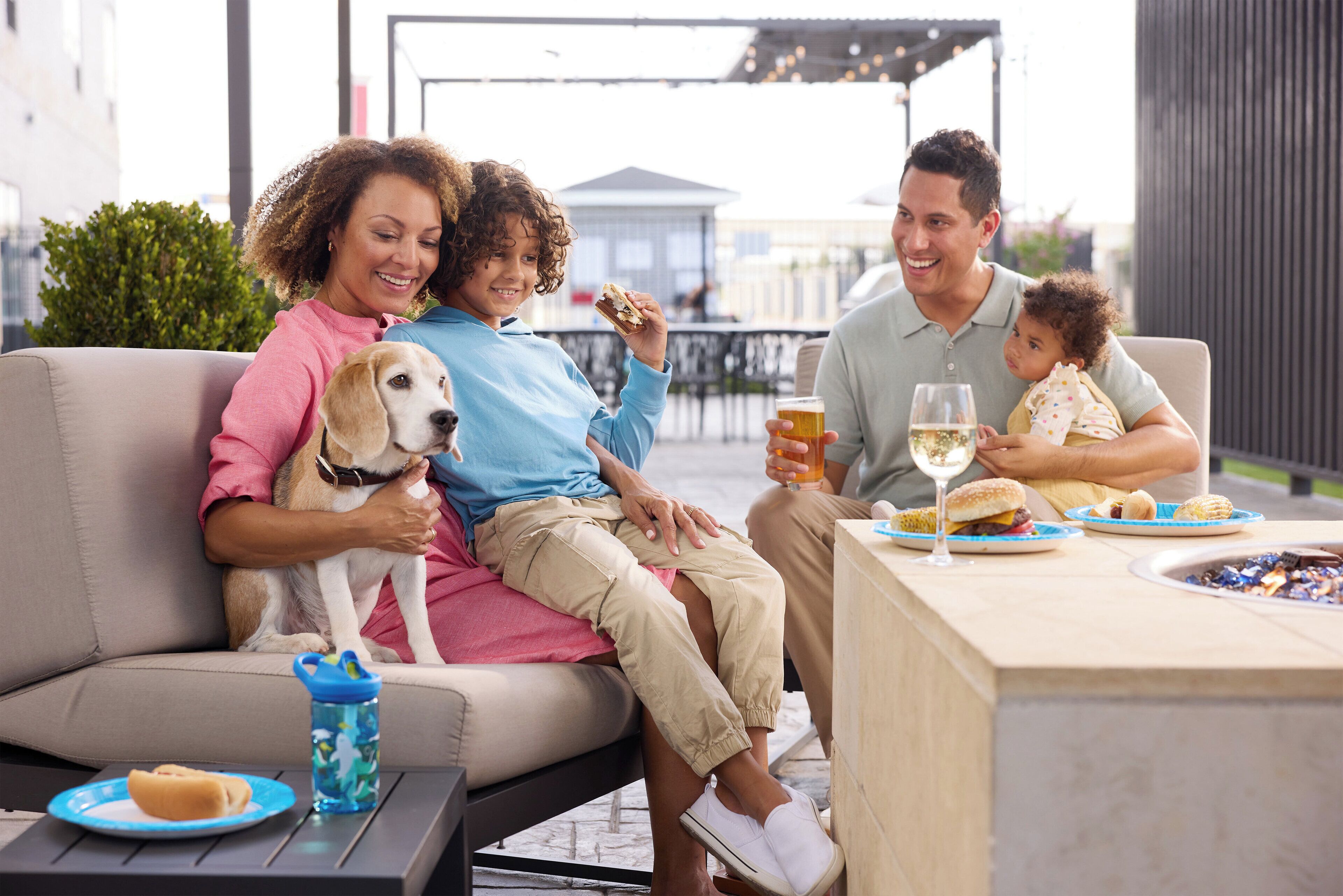 A family dining outdoors with a dog, a table with food and drinks, and a patio setting.