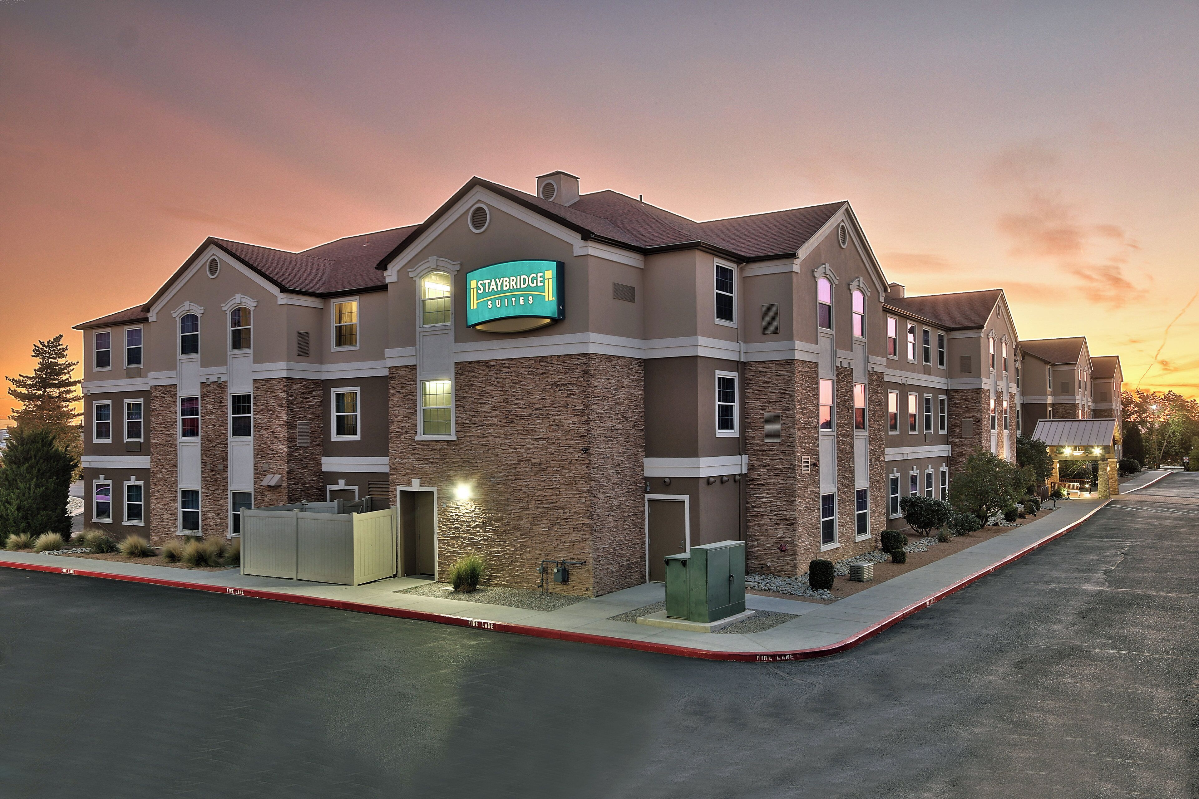 Un hotel Staybridge Suites con fachada de piedra, múltiples ventanas y una entrada bien iluminada.