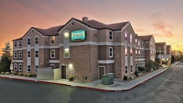 Un hotel Staybridge Suites con fachada de piedra, múltiples ventanas y una entrada bien iluminada.