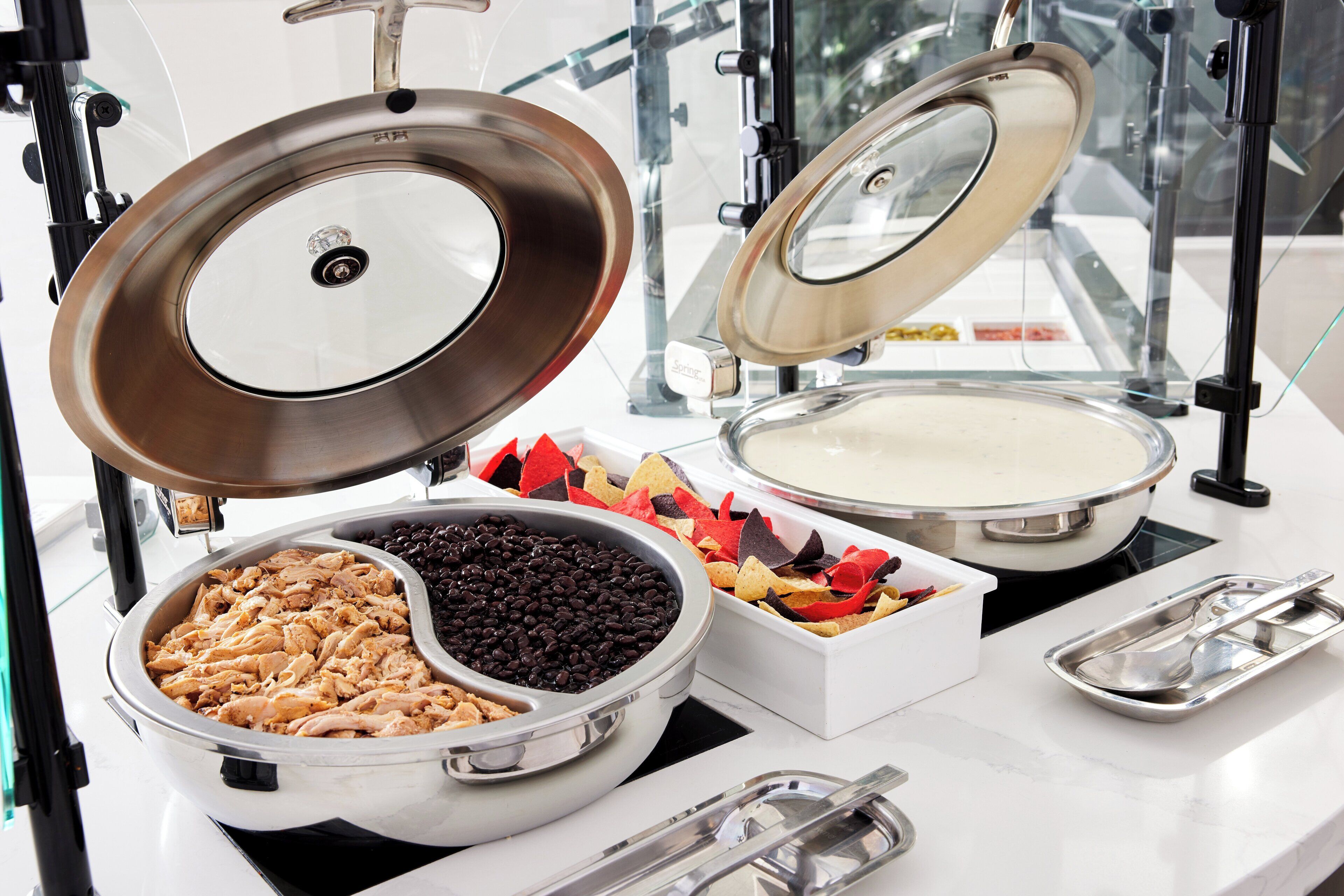 A buffet setup with various food items including beans, chicken, and tortilla chips.