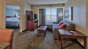 A hotel room with a bed, a sofa, a desk, a TV, and a window with curtains.