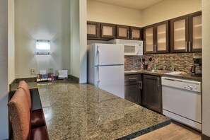 A kitchen with granite countertops, a refrigerator, microwave, dishwasher, and dark wooden cabinets. - Staybridge Suites North - Albuquerque by IHG (Albuquerque)