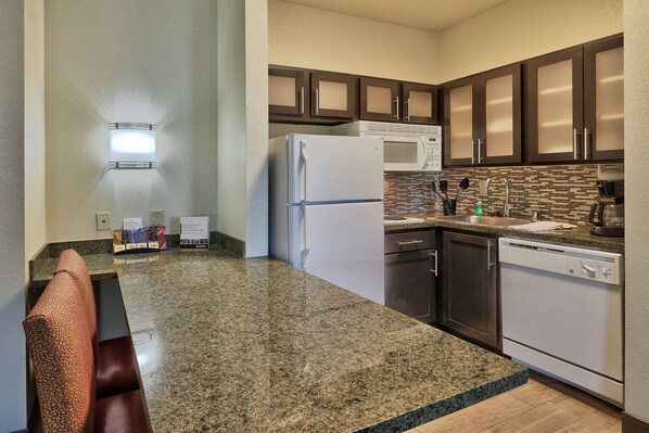 A kitchen with granite countertops, a refrigerator, microwave, dishwasher, and dark wooden cabinets.
