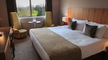 Habitación de hotel con una cama grande, dos sillones, una mesita de noche con lámpara y vistas al exterior a través de una ventana.