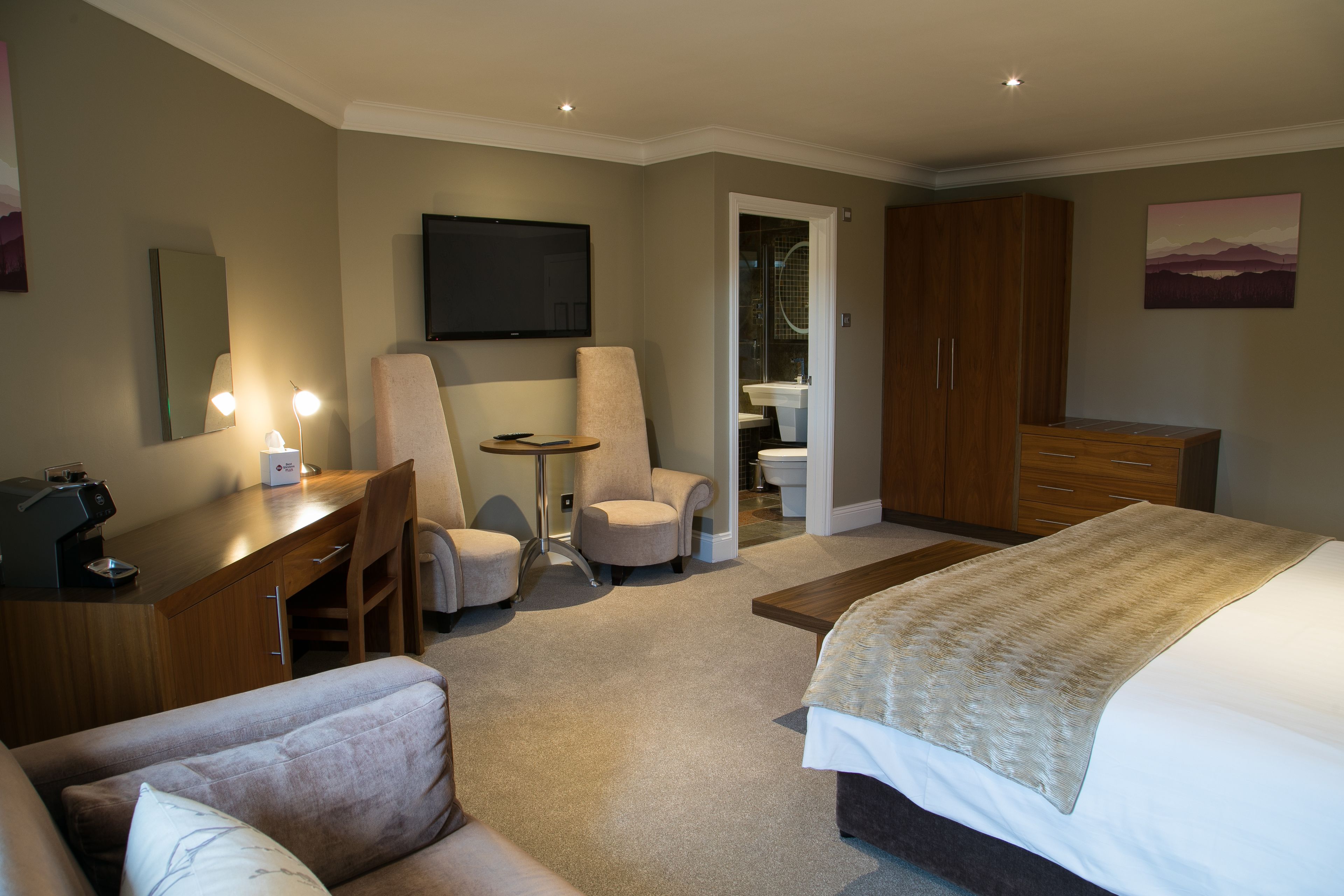 Ein Hotelzimmer mit einem Bett, einem Schreibtisch mit Computer, einem Stuhl, einem Fernseher und einem Kleiderschrank.