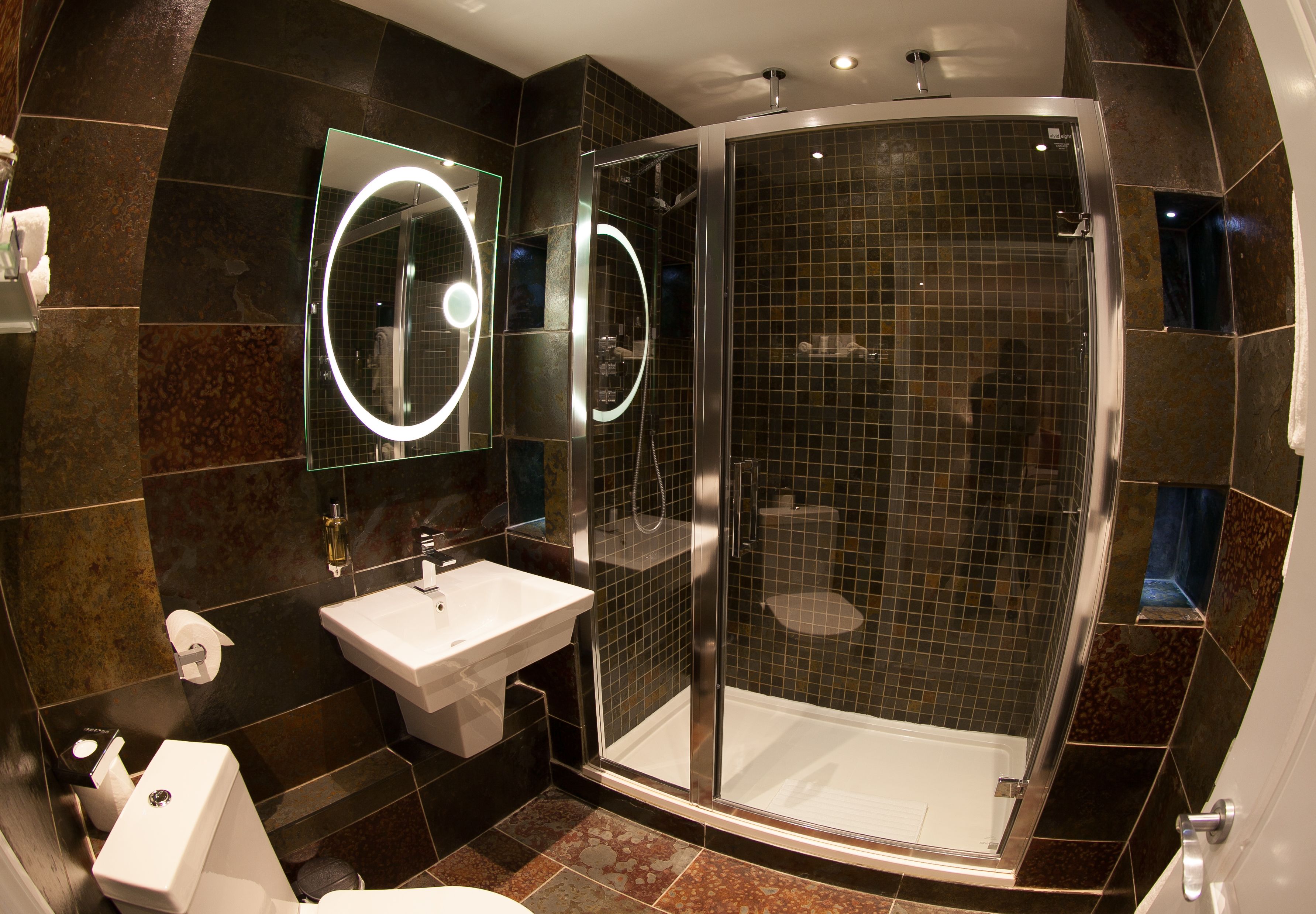 A modern bathroom with a glass-enclosed shower, a sink, and two illuminated mirrors.