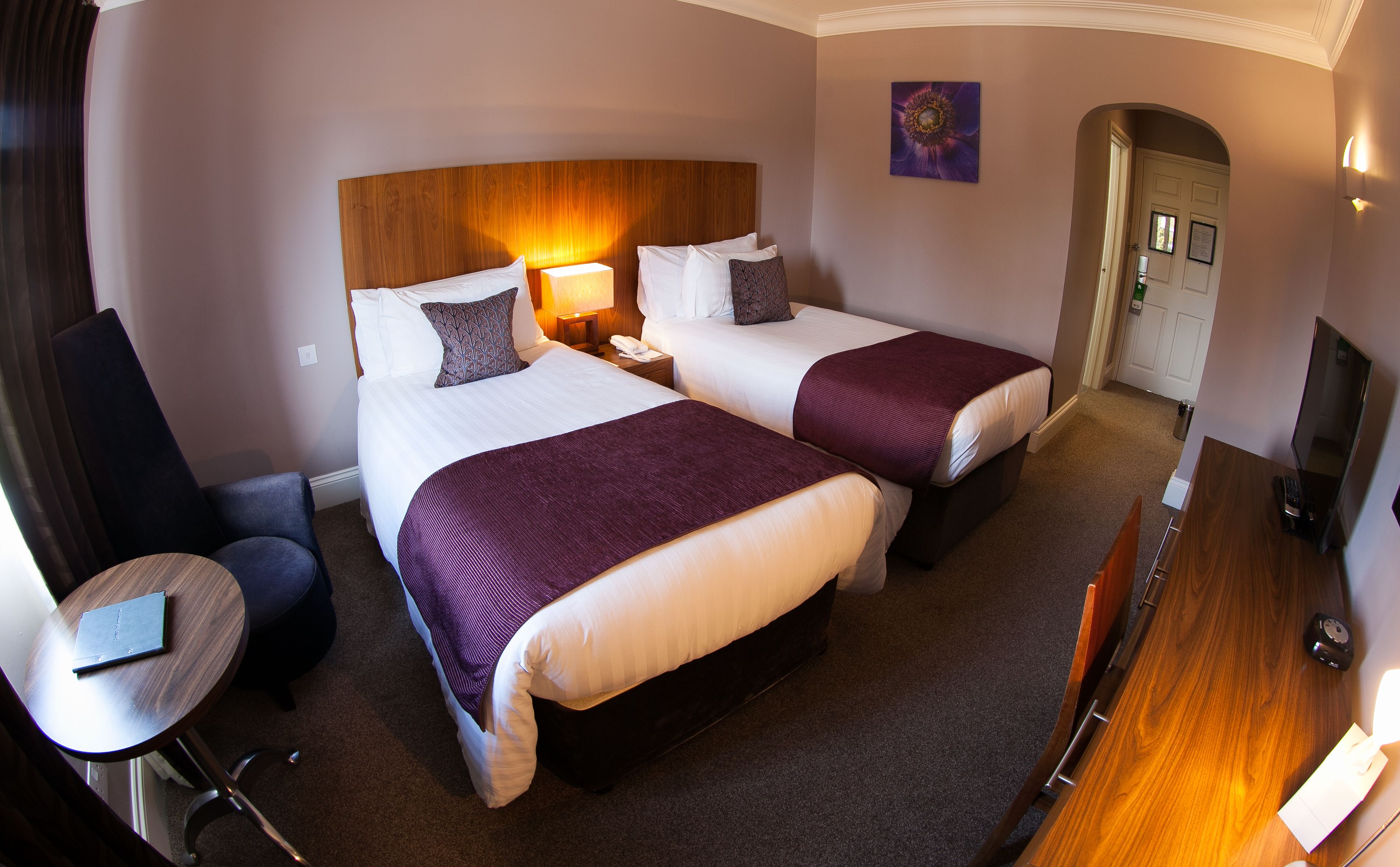 A hotel room with two beds, a desk, a chair, and a TV.