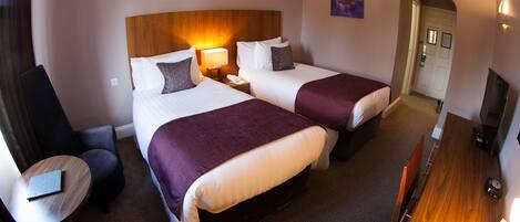 A hotel room with two beds, a desk, a chair, and a TV.