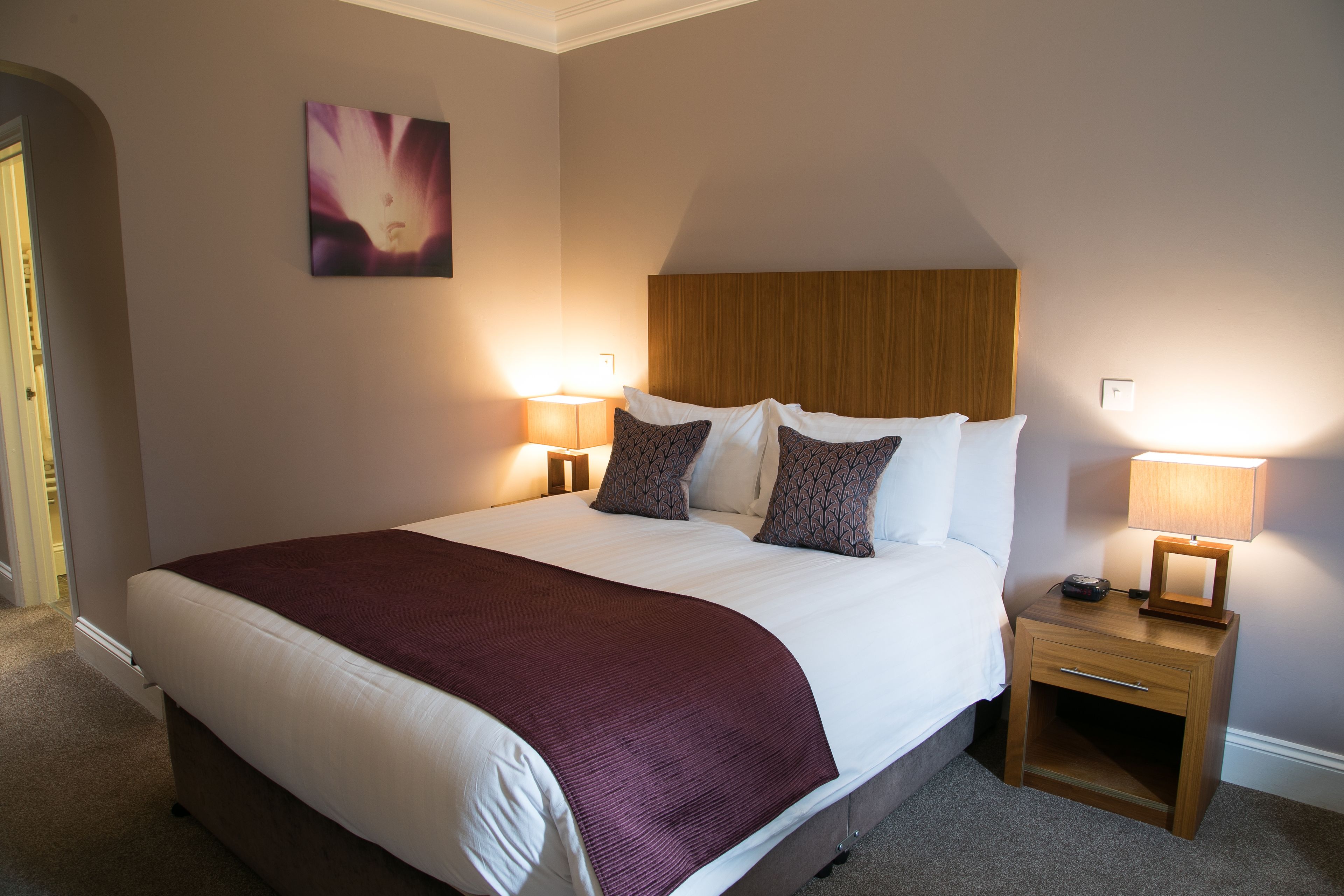A neatly made bed with a wooden headboard, two bedside tables with lamps, and a single artwork on the wall.