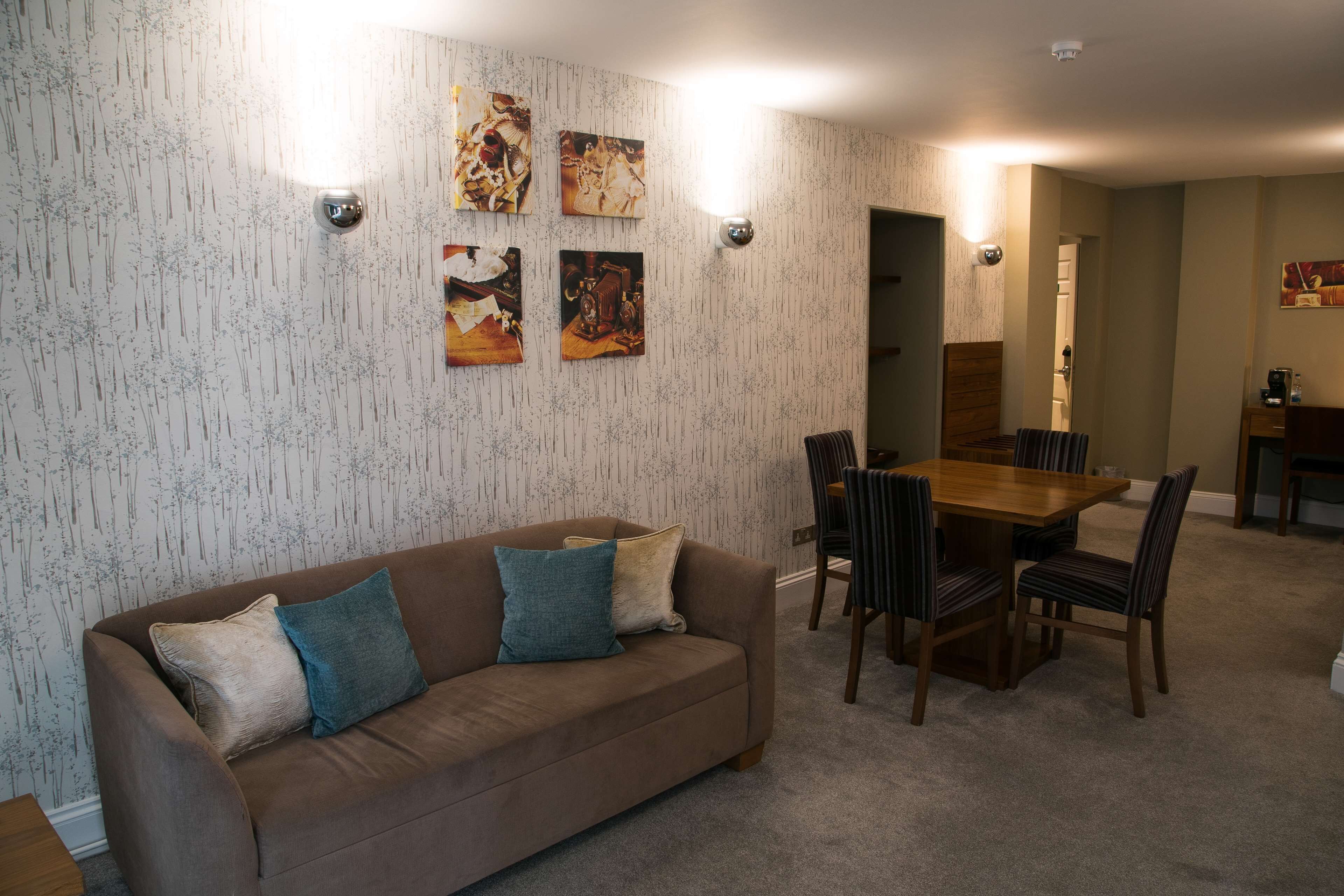 Una sala de estar con un sofá marrón, una mesa de comedor con sillas y una zona de cocina al fondo.