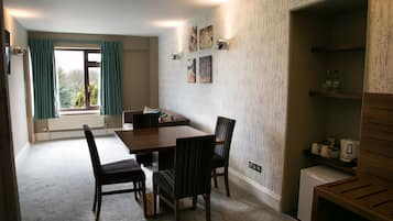 Un comedor con una mesa y sillas de madera, una ventana con cortinas y un estante empotrado con utensilios de cocina.
