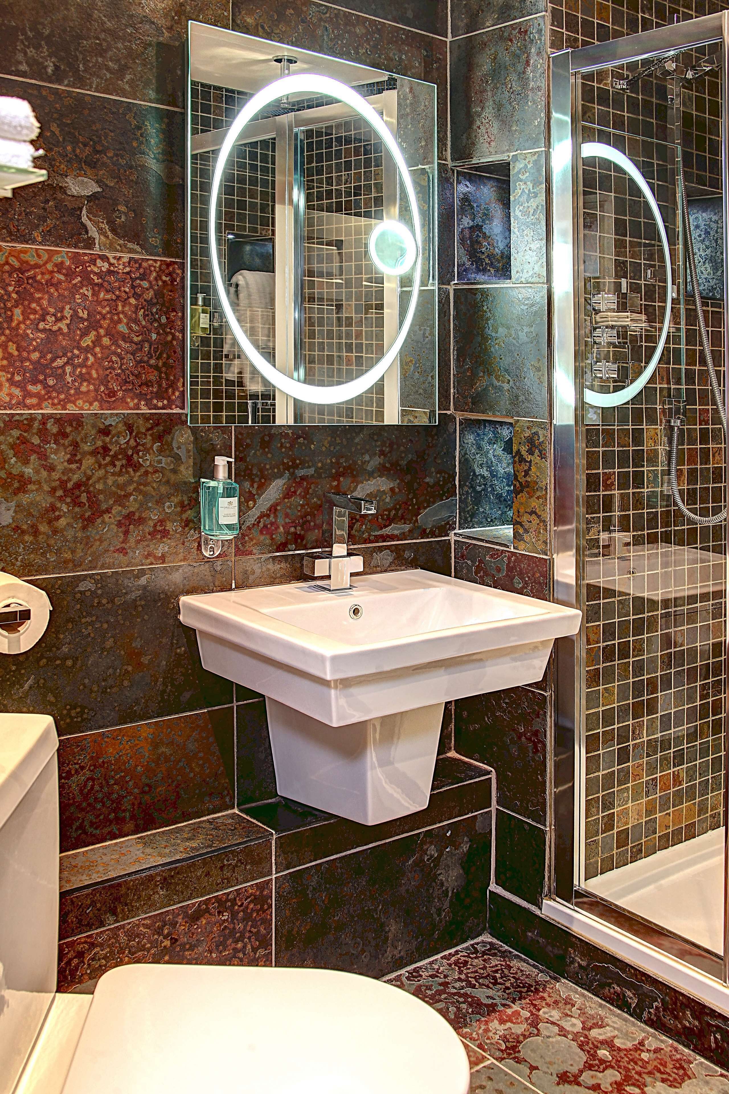 Une salle de bain avec un lavabo blanc, un miroir avec éclairage intégré et un espace douche.