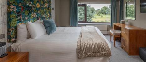 Ein Schlafzimmer mit einem großen Bett, einer Holzkommode, einem Schreibtisch und Blick auf einen Garten durch ein Fenster.
