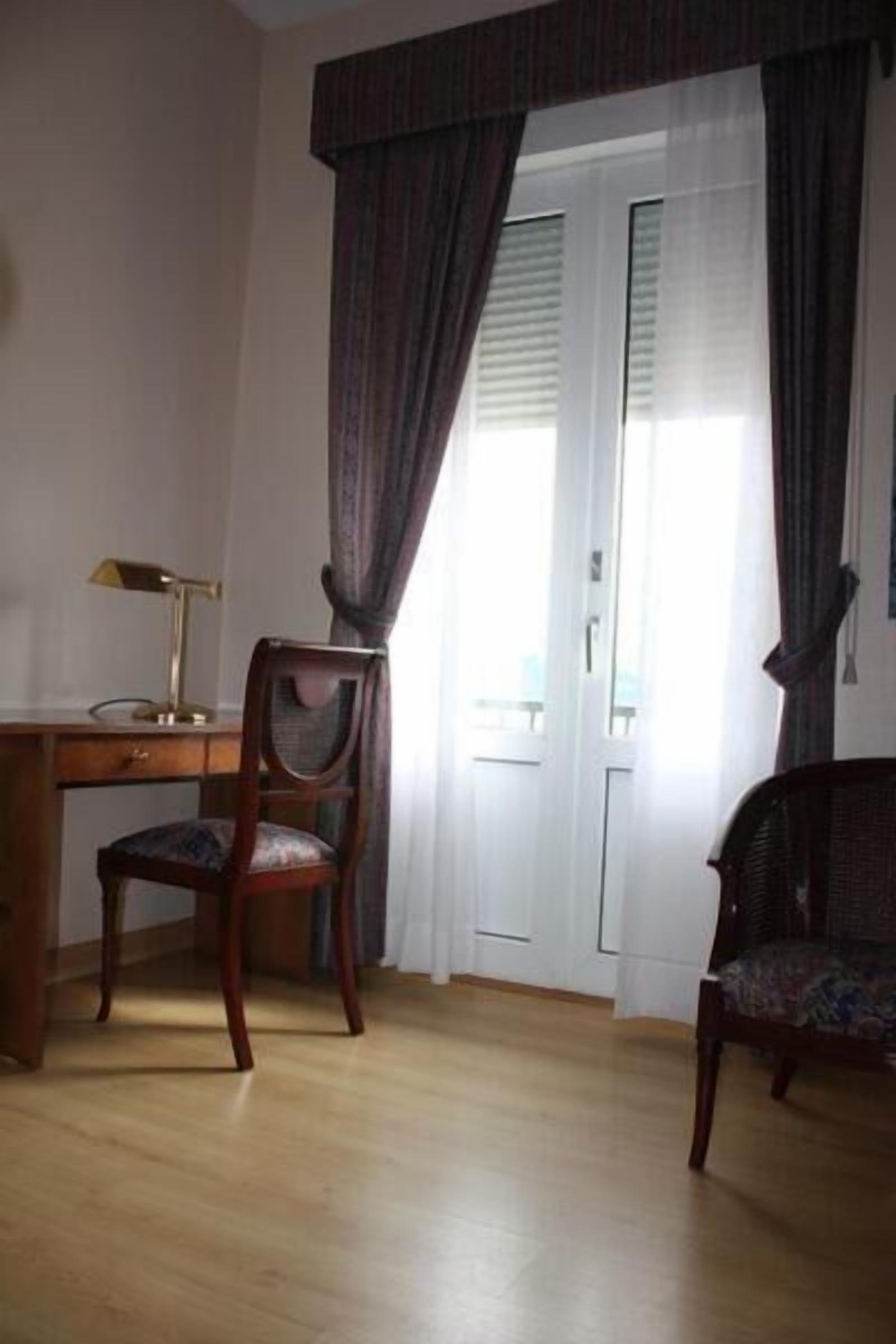 A room with a wooden desk, two chairs, a lamp, and a door with curtains.