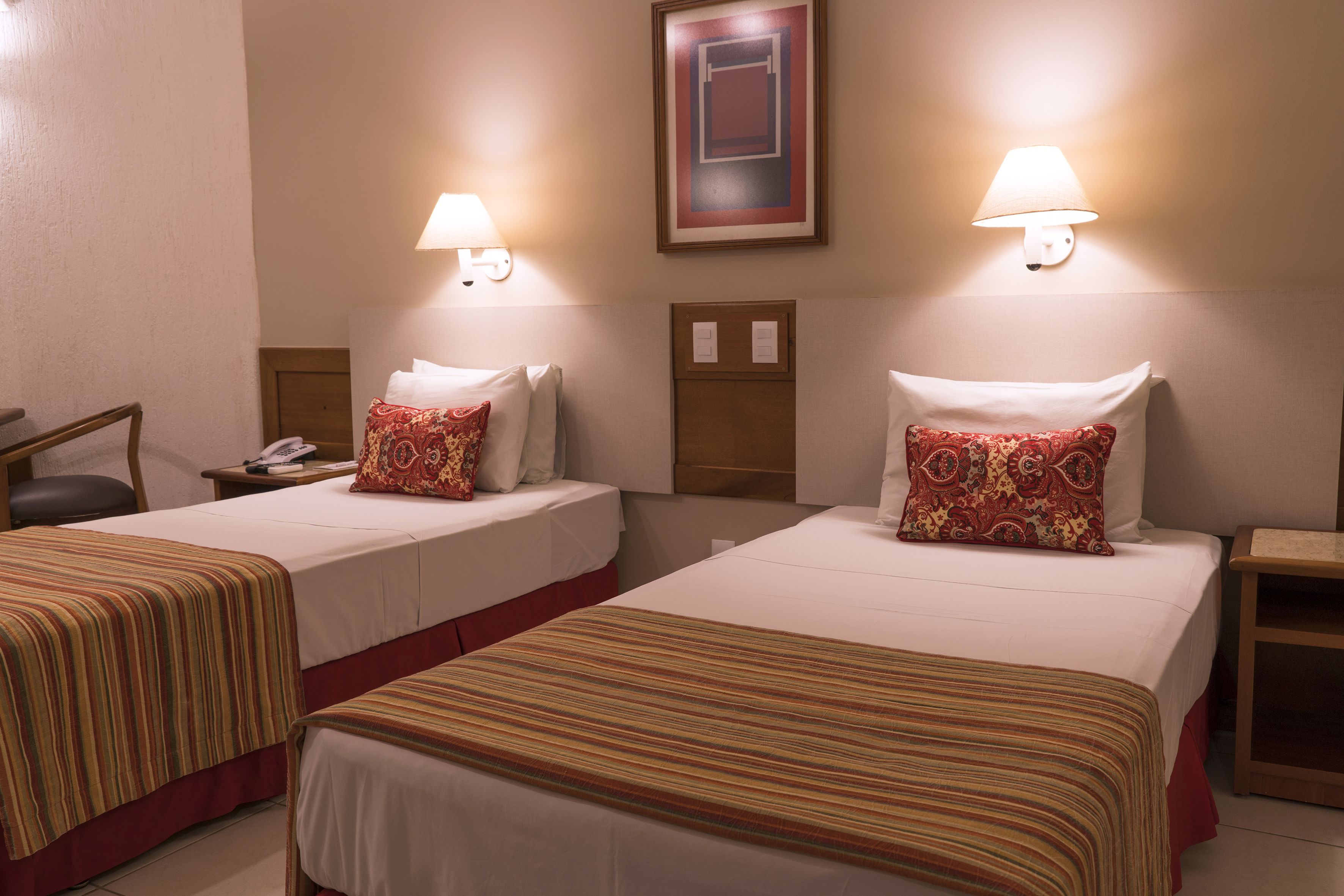 Two single beds with striped bedding, bedside lamps, and a framed artwork on the wall.