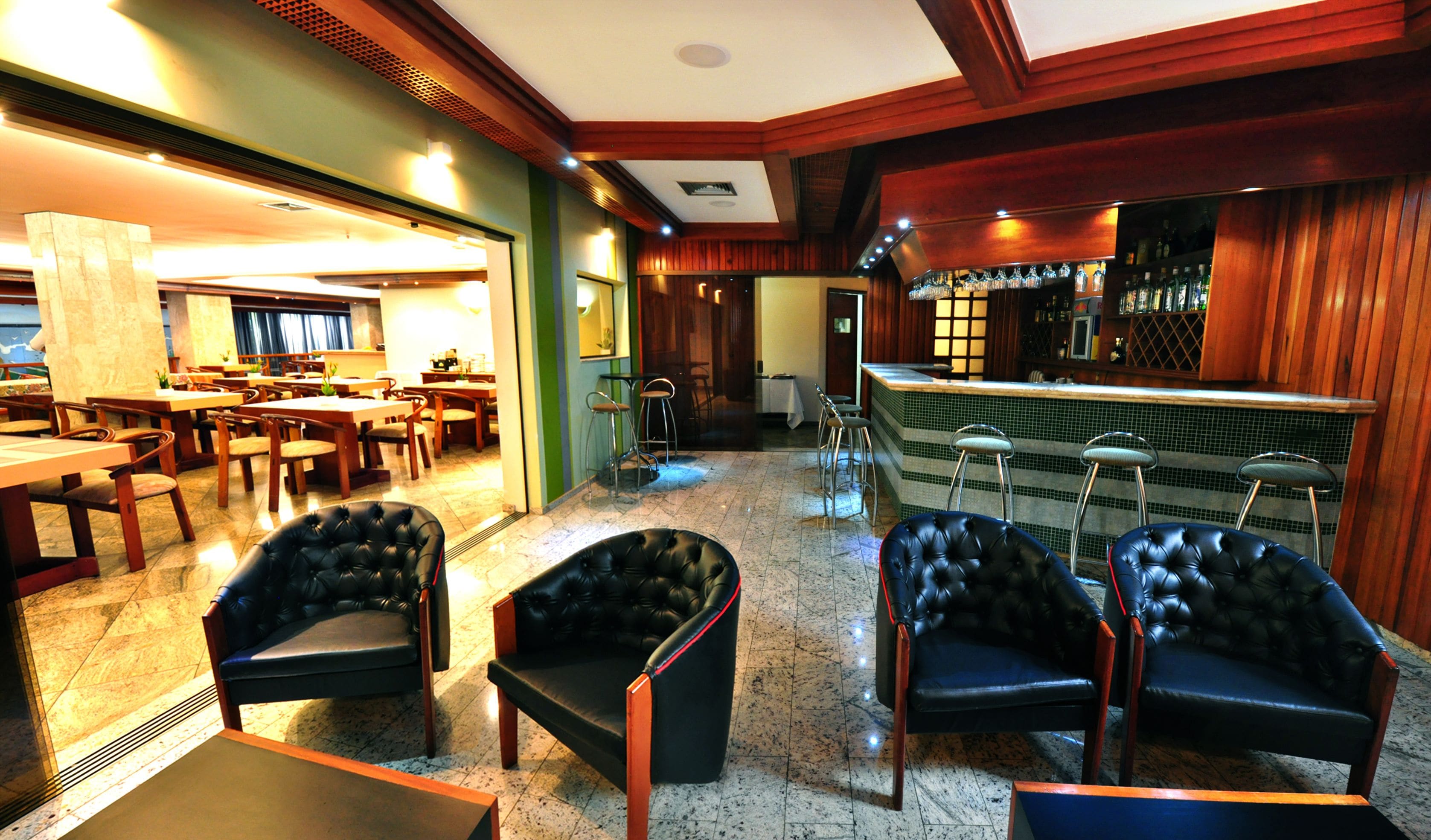 A spacious lobby with leather armchairs, a bar area with stools, and a dining section with tables and chairs.