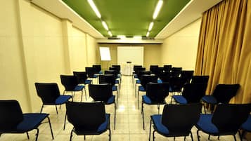 Un salón de conferencias con filas de sillas negras con cojines azules, una pantalla de proyector al frente y un techo verde.