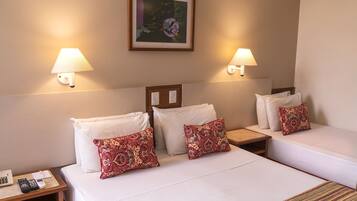 Habitación de hotel con dos camas, cada una con sábanas blancas y almohadas rojas estampadas. Hay dos lámparas de pared a cada lado de las camas, y un cuadro enmarcado sobre el cabecero.
