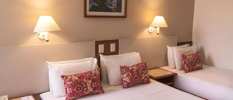 A hotel room with two beds, each with white linens and red patterned pillows. There are two wall-mounted lamps on either side of the beds, and a framed picture above the headboard.