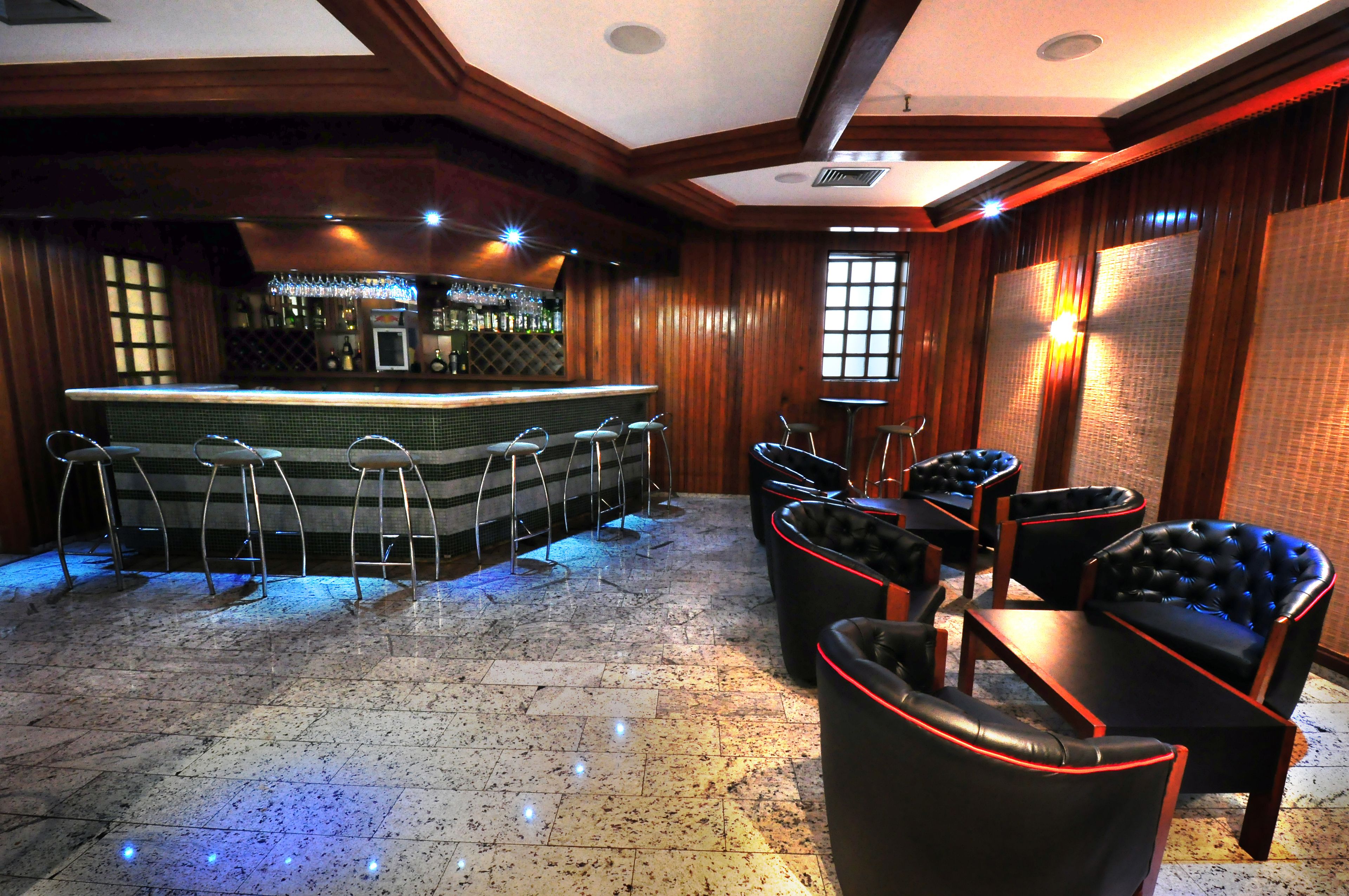 A bar area with a counter, stools, and leather chairs.