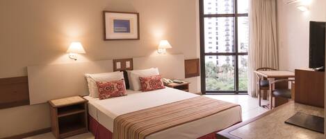 Una habitación de hotel con cama, mesitas de noche, escritorio, silla y televisor.