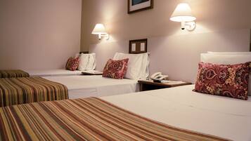 A hotel room with two single beds, each with a striped bedspread and a patterned pillow. There are wall-mounted lamps on either side of the beds, and a framed picture above the headboard.