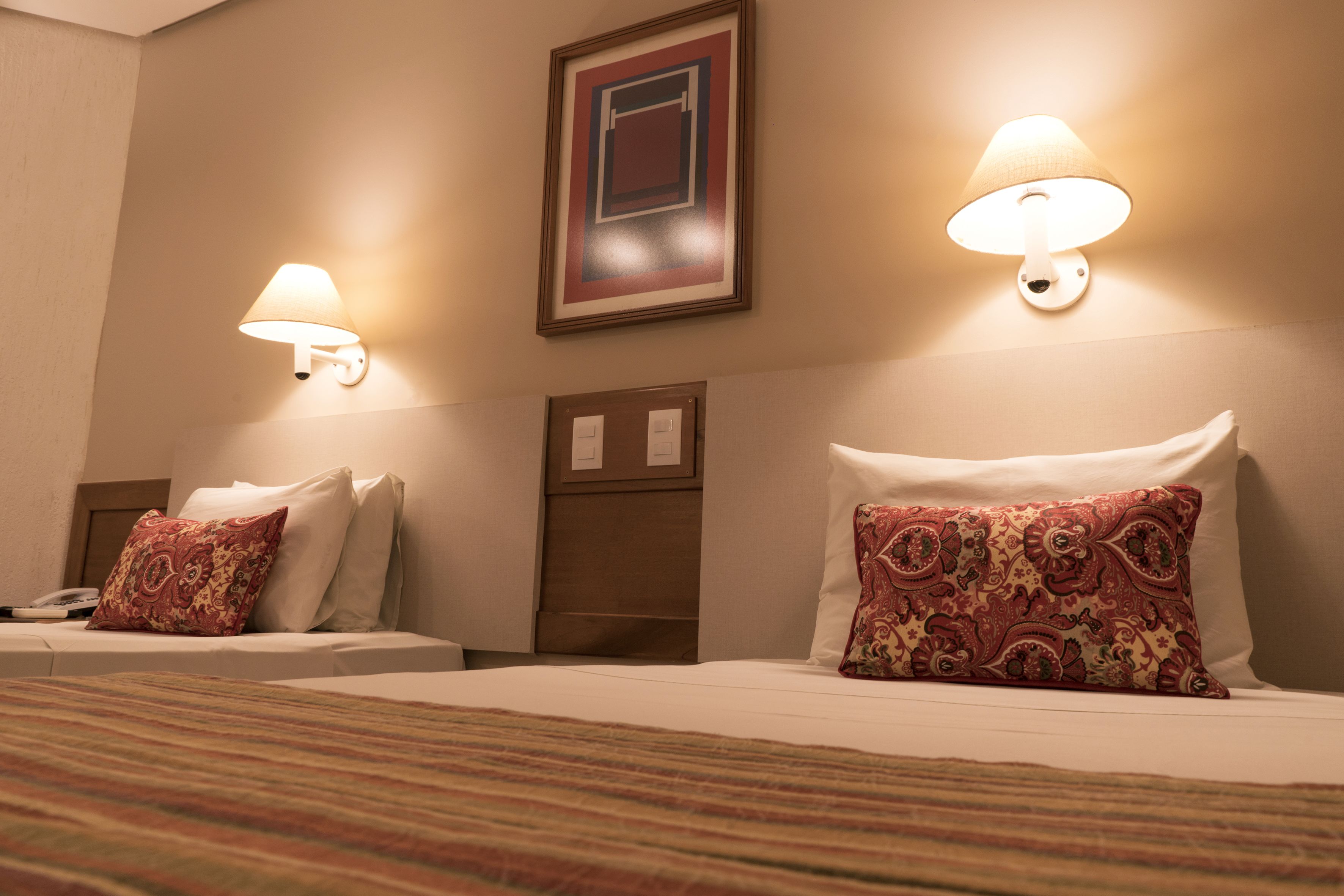 Quarto de hotel com duas camas, cada uma com travesseiro e uma luminária fixada na parede.