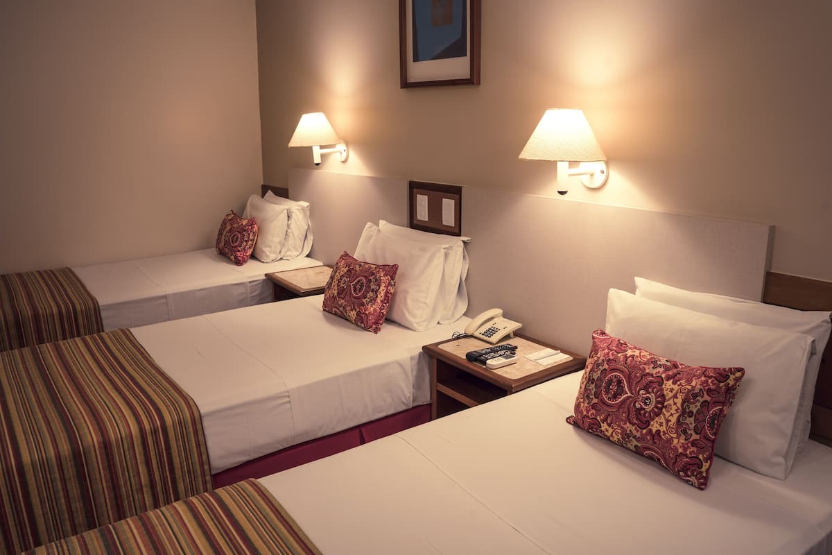 Habitación de hotel con dos camas individuales, cada una con una almohada y una mesita de noche con lámpara y teléfono.