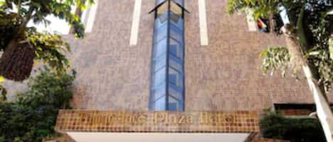 A hotel entrance with a modern design, featuring a prominent vertical glass facade and a tiled roof.