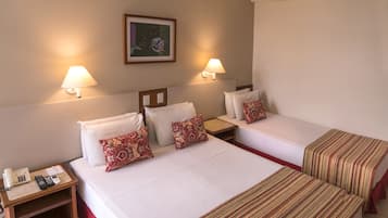 Quarto de hotel com duas camas, cada uma com travesseiro e mesa de cabeceira com abajur e telefone.