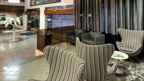 Un hall d’entrée avec des fauteuils à rayures, un canapé, un tableau et une grande fenêtre avec des rideaux.