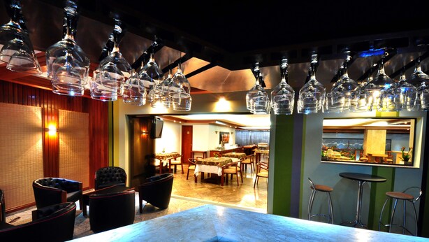 Un espace bar doté d’un comptoir en marbre, de verres à vin suspendus et d’un coin salon avec des chaises et des tables.