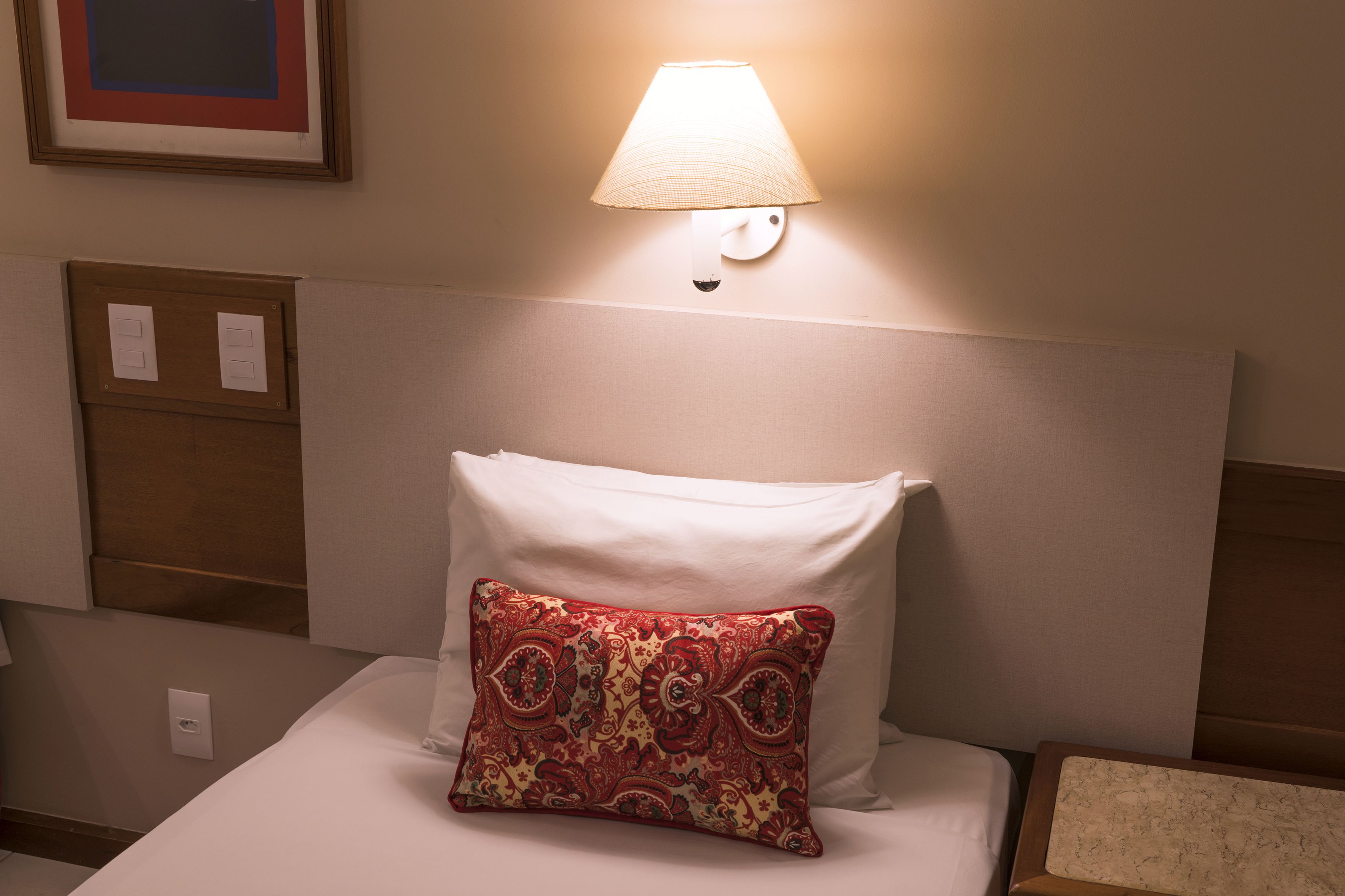 Habitación de hotel con una cama, una lámpara de pared y un cuadro enmarcado sobre la cama.