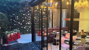 A cozy outdoor seating area with glass walls, a variety of seating options, and a decorative flower wall.