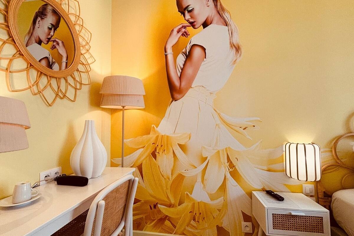A room with a bed, a bedside table with a lamp, a chair, a mirror, and a dresser.