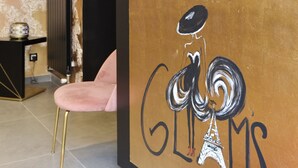 A reception desk with a decorative vase, a pink chair, and a wall with the word "GLAMS" and an illustration of the Eiffel Tower. - Le Glam's Hôtel (Paris)