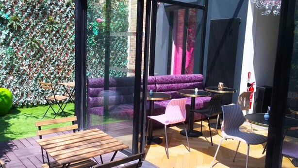 A patio area with a wooden bench, purple seating, and small round tables. - Le Glam's Hôtel (Paris)