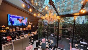 A modern cafe with a TV displaying a sports event, a variety of food and drink options, and a cozy seating area with tables and chairs. - Le Glam's Hôtel (Paris)