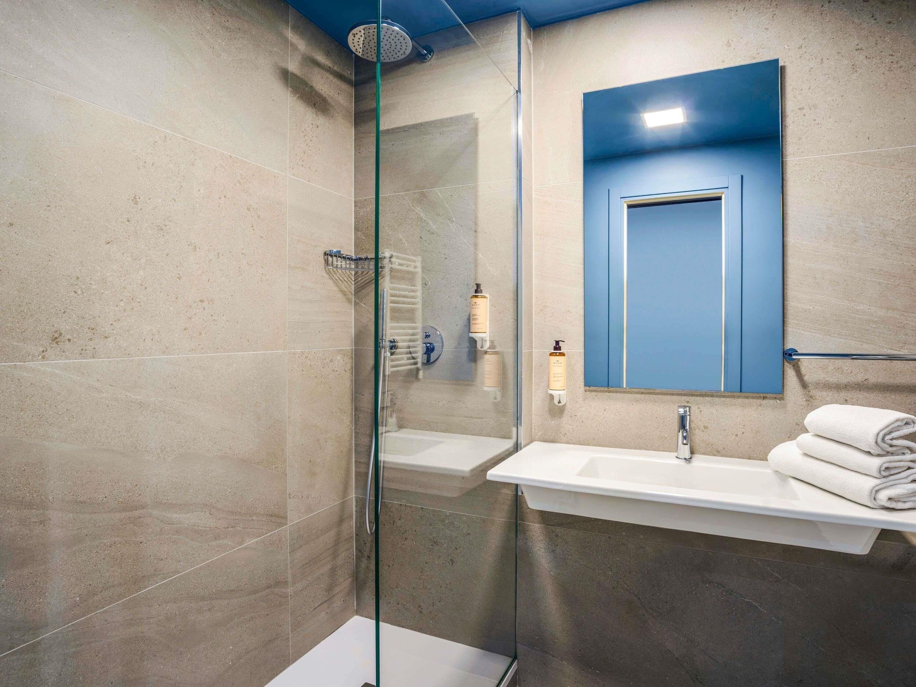 Een moderne badkamer met een douchecabine van glas, een wastafel en een spiegel met een blauwe deur.