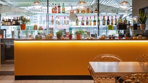 A bar area with a yellow counter, shelves of liquor bottles, and potted plants. - Mercure Milano Agrate Brianza (Agrate Brianza)