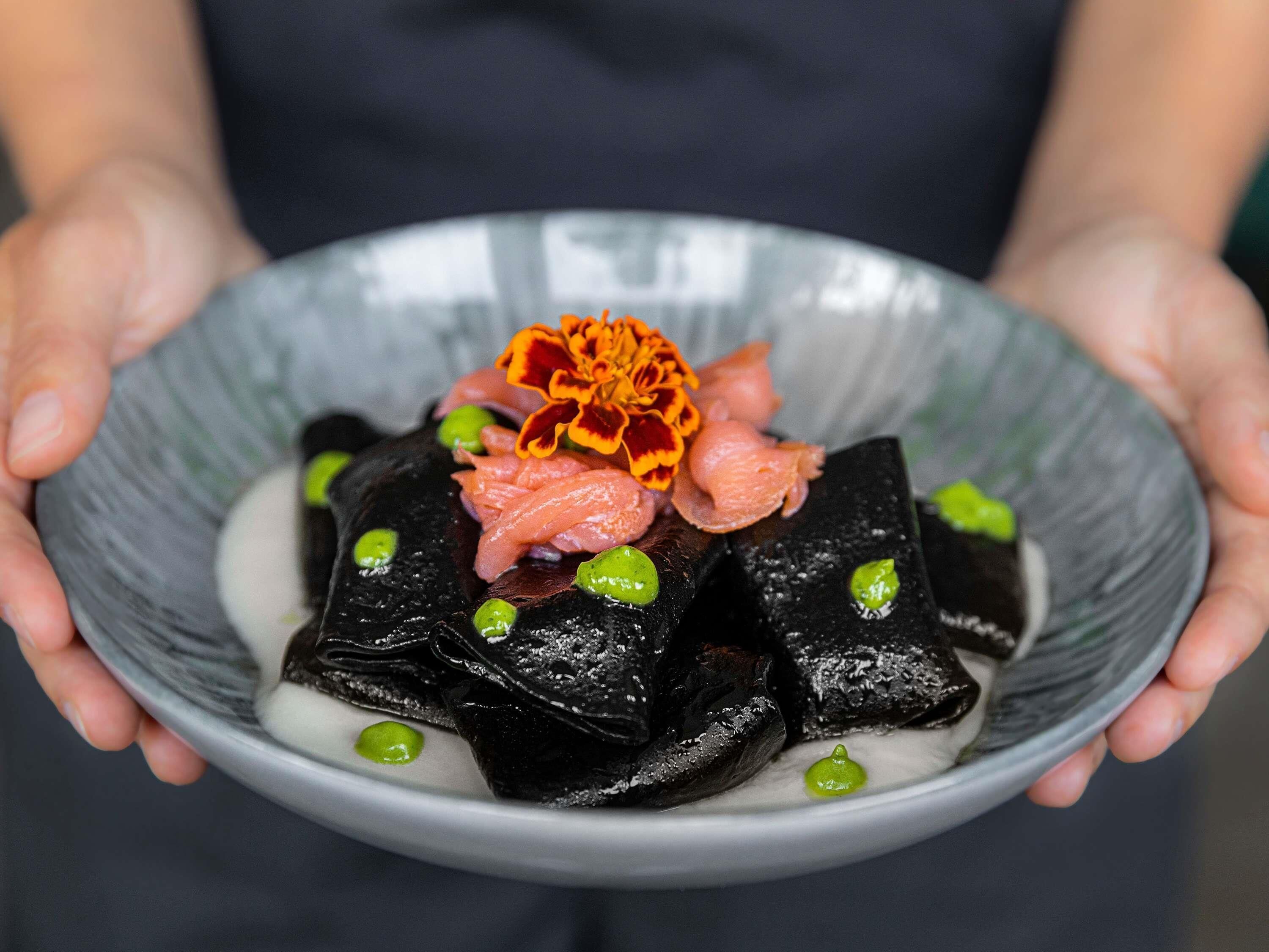 A bowl of food with black items, green peas, and orange flowers.