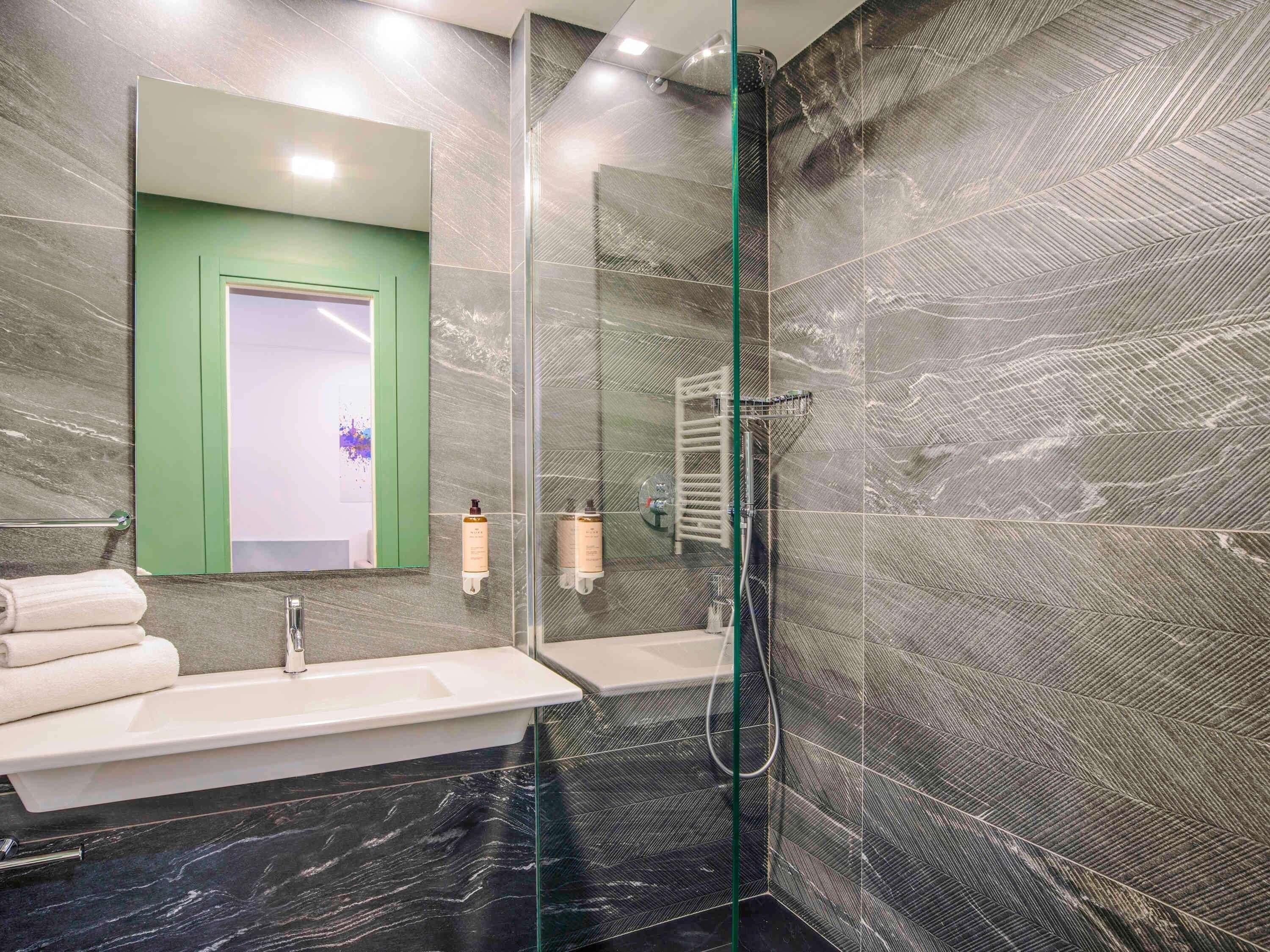 A modern bathroom with a glass shower enclosure, a green door, and marble flooring.