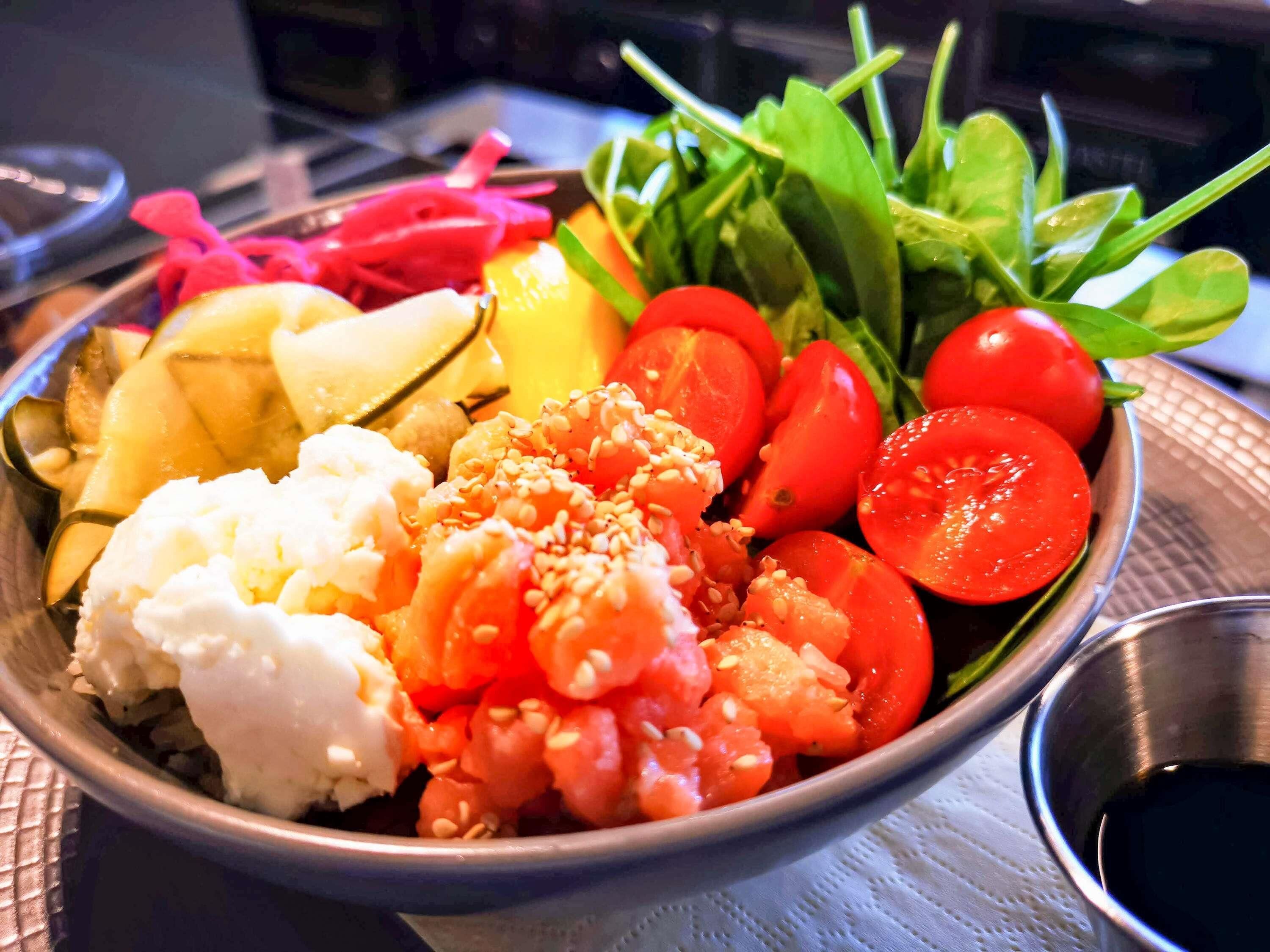 A bowl of salad with various vegetables and a small bowl of dressing.