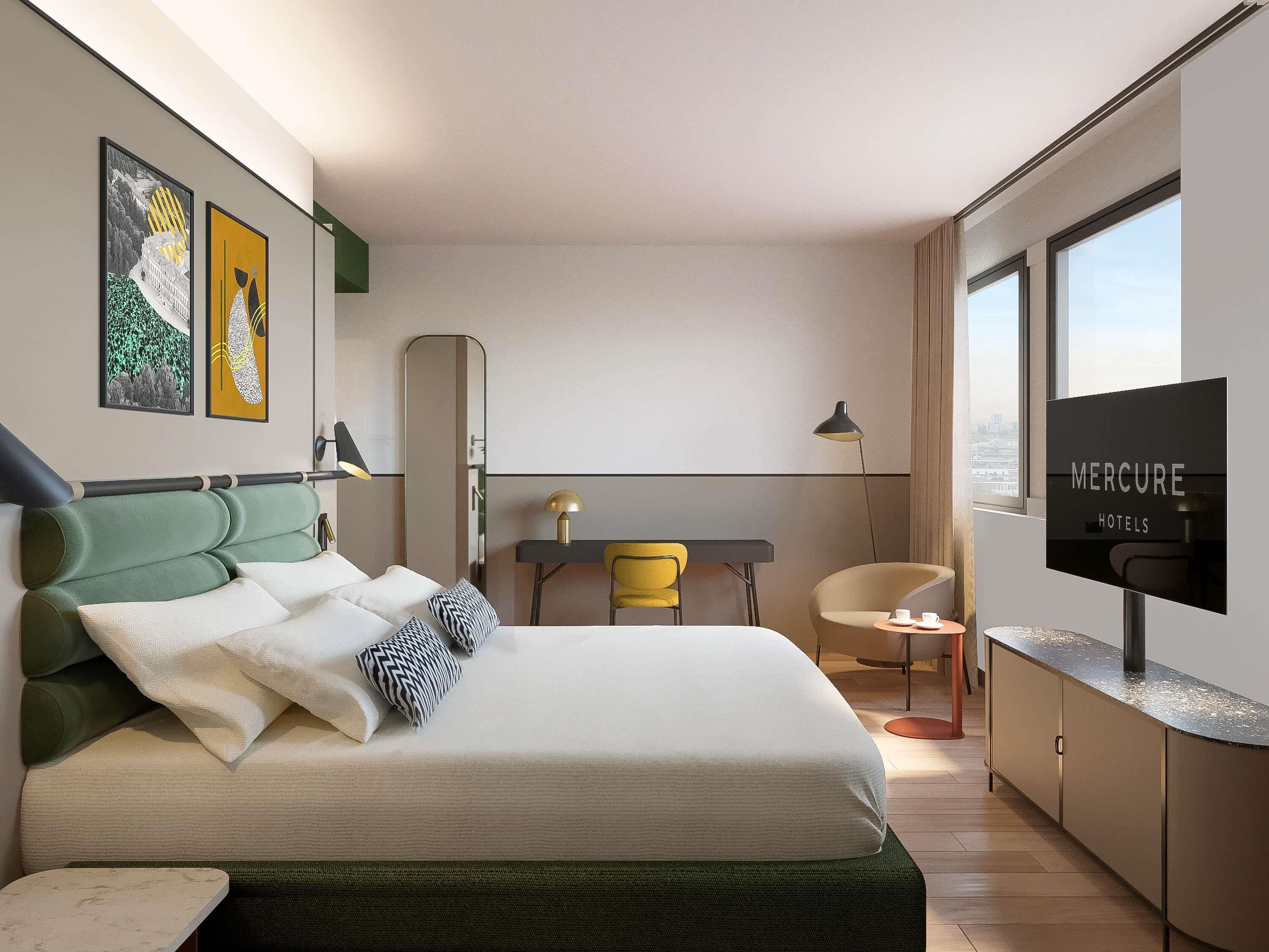 Une chambre d’hôtel moderne équipée d’un lit, d’un bureau, d’une chaise et d’un téléviseur affichant le logo « MERCURE HOTELS ».
