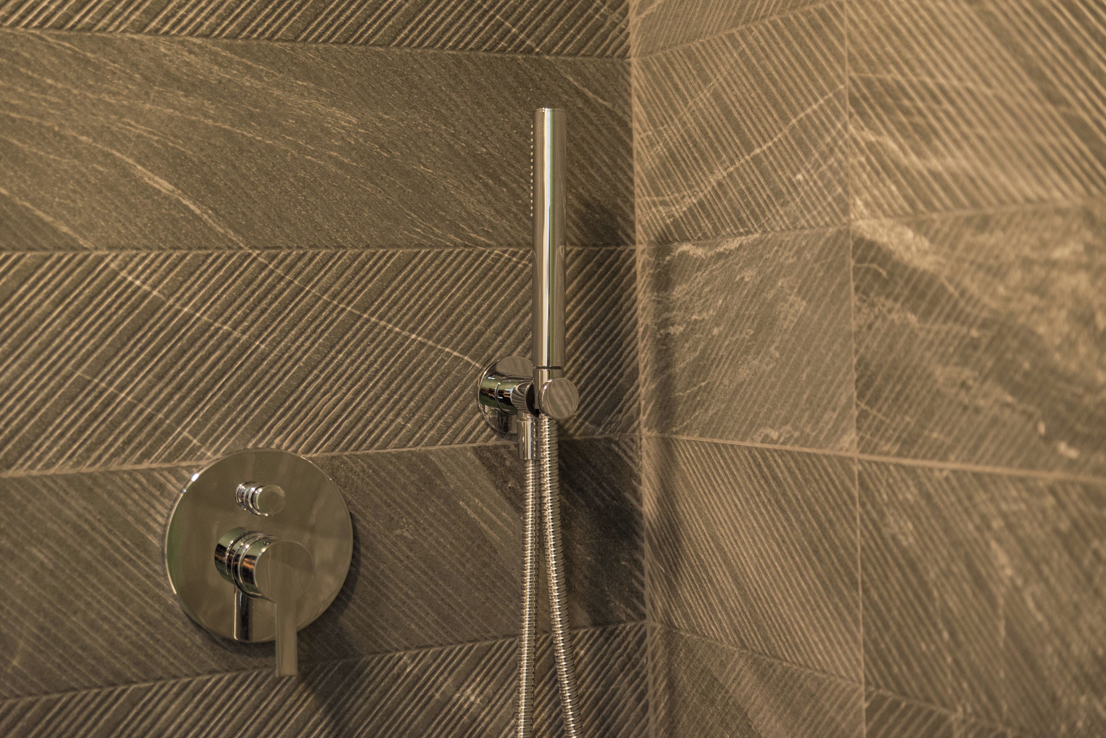 Ducha con grifo y manguera de cromo, frente a una pared con textura.