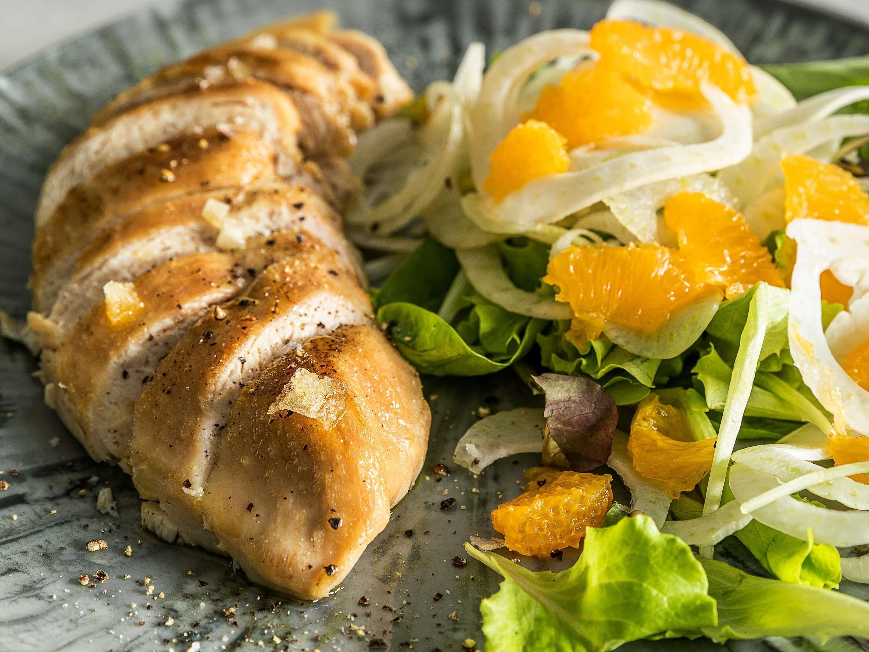 Une assiette contenant des tranches de poulet, des quartiers d’orange et une salade verte.