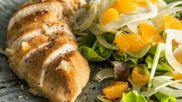 Une assiette contenant des tranches de poulet, des quartiers d’orange et une salade verte.